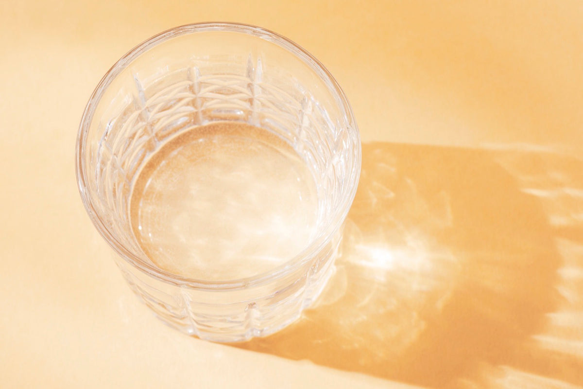 Vaso de agua sobre una mesa naranja, con una sombra larga de luz cálida