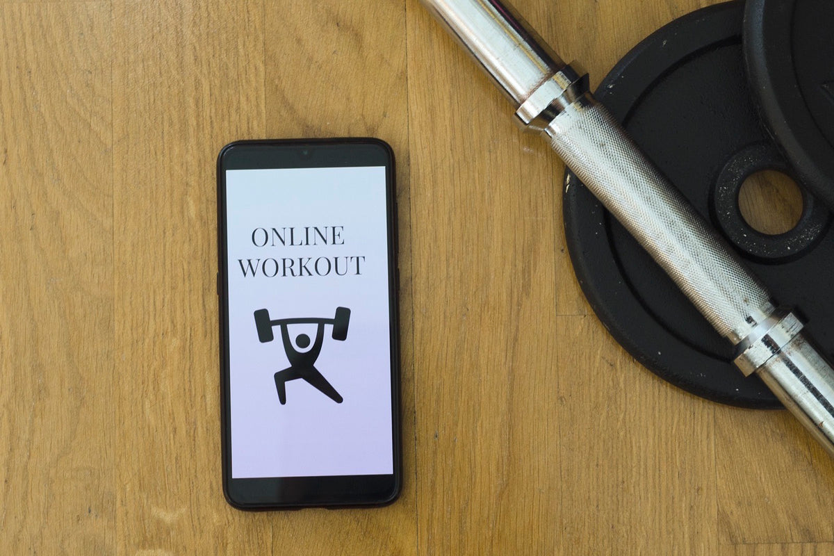 Celular con una app de entrenamiento junto a una barra y discos sobre madera