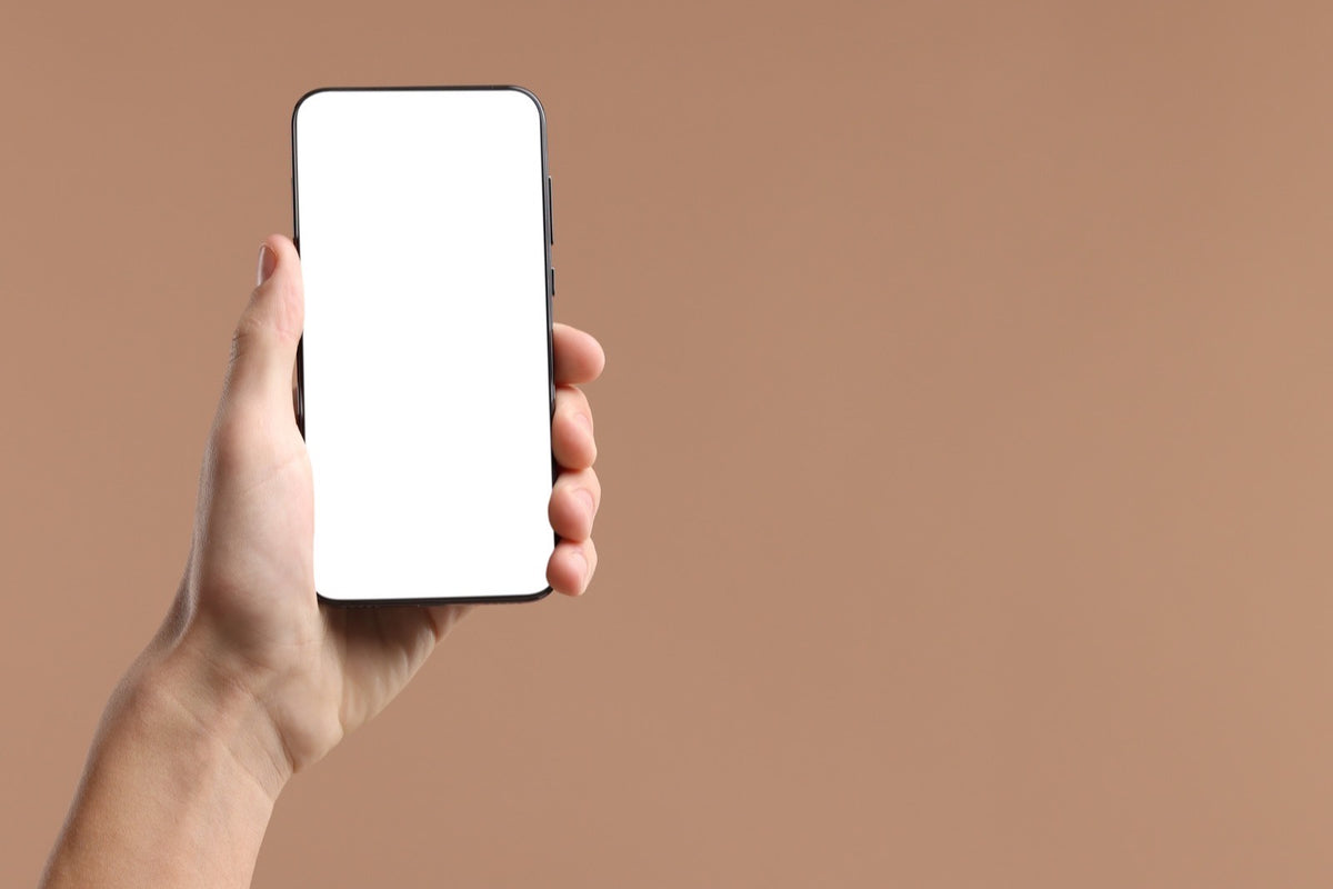 Mano sosteniendo un celular con la pantalla en blanco sobre un fondo terracota