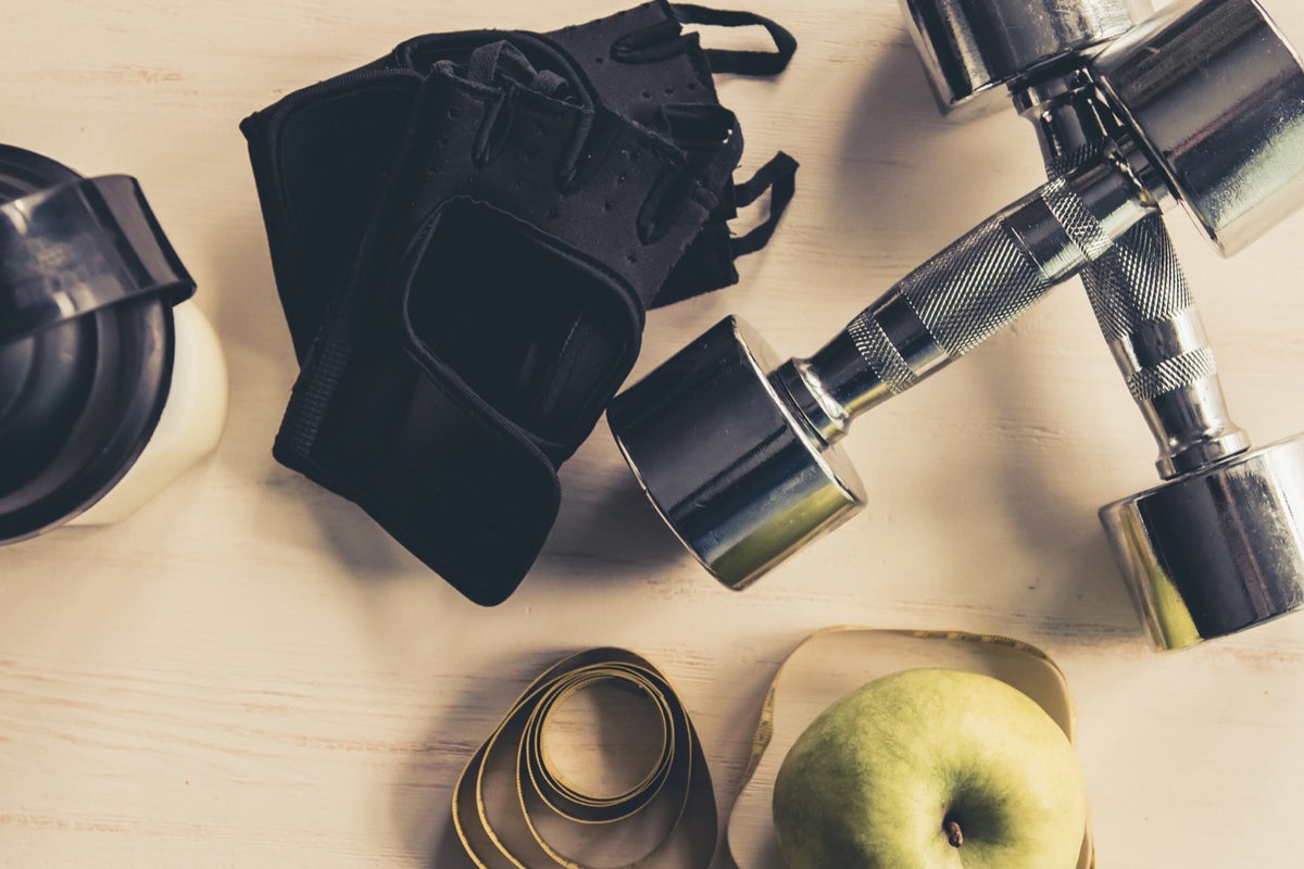 Mancuernas junto a una manzana y una botella sobre una mesa de madera clara, vistas desde arriba
