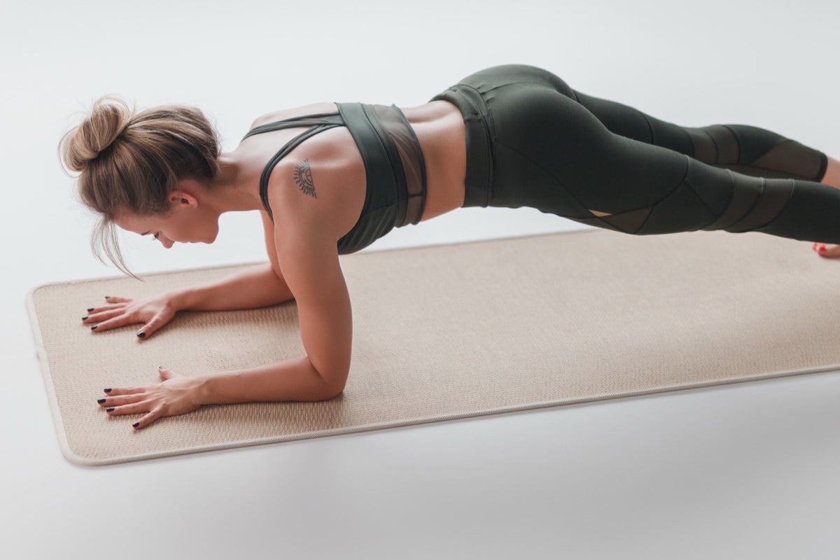 Mujer sosteniendo una plancha sobre una colchoneta en una sala luminosa