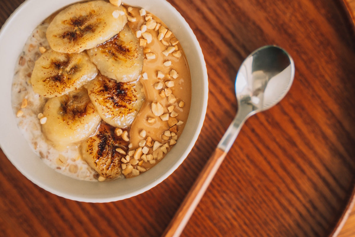 Bol de avena con plátano y nueces sobre una bandeja de madera, visto desde arriba