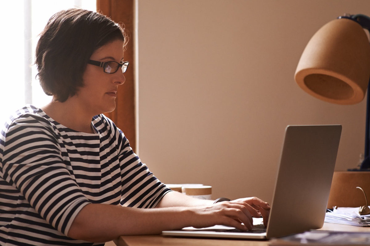 Mujer trabajando en su laptop en un escritorio de madera, junto a una ventana
