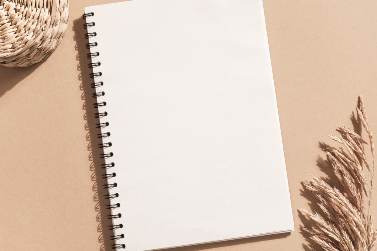 Cuaderno en blanco abierto sobre un fondo beige, junto a espigas secas